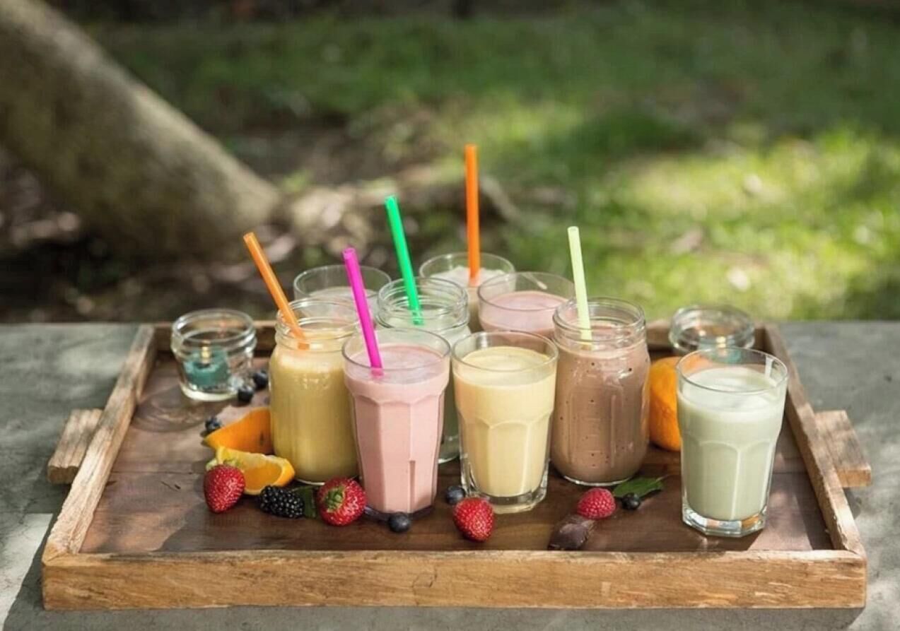 A wooden tray with various smoothie glasses and fresh fruits.