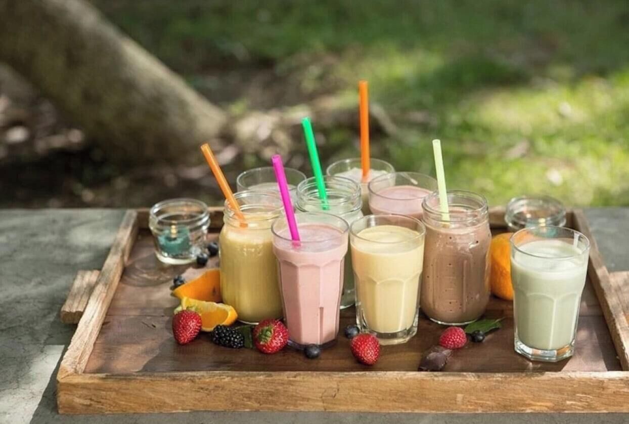 Una bandeja de madera con vasos de batidos y frutas frescas.