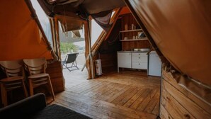 Un hébergement sous tente doté d’un plancher en bois, d’une petite kitchenette et d’une chaise à l’extérieur.