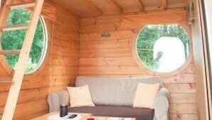 A cozy cabin interior with a wooden interior, a loft bed, a small table, and two round windows. - ZEcamping 4 étoiles familial piscine chauffée roulotte 9m2 2 pers (Estipouy)