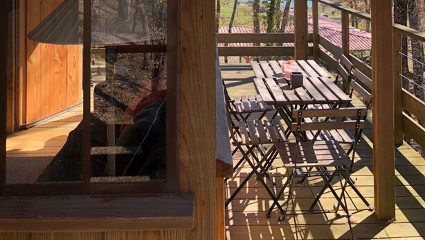 Una cabaña de madera con un porche cubierto y vistas del paisaje circundante.