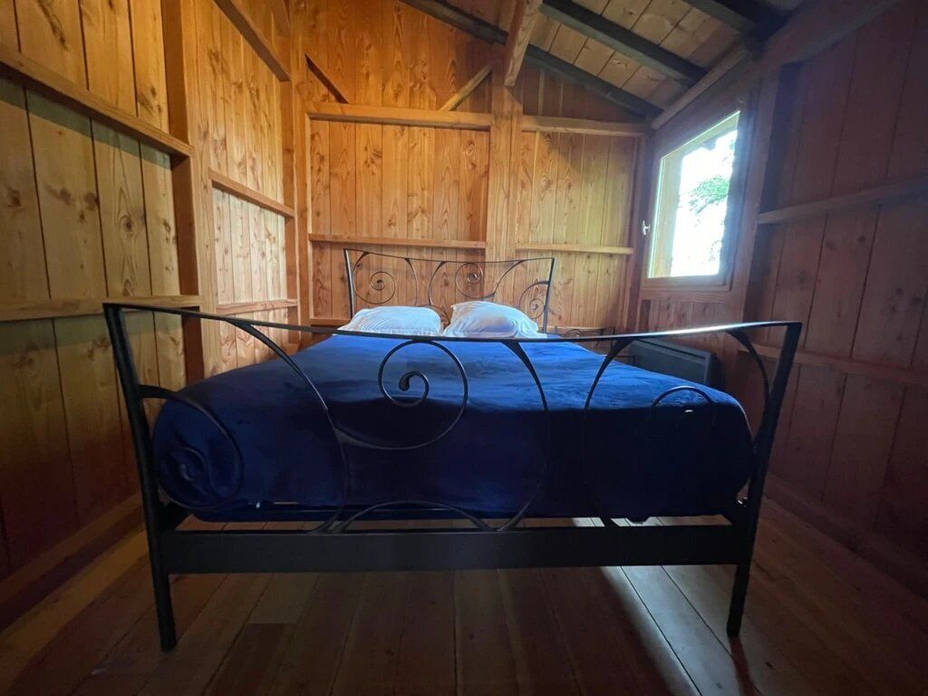 A wooden cabin room with a metal bed frame and a blue mattress.