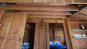 Interior de una cabaña de madera con cama en altillo, una pequeña kitchenette y ventana que deja entrar luz natural.