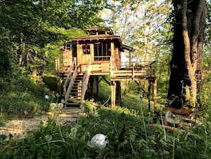 A wooden cabin with a staircase leading up to it, surrounded by trees and dandelions. - ZEcamping 4 étoiles familial piscine chauffée locatif BBQ 29m2 (Estipouy)