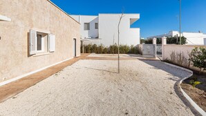 Un bâtiment moderne avec une cour en gravier, un petit arbre et un ciel bleu dégagé.