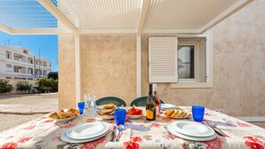 Un espace de restauration en plein air avec une table dressée pour deux personnes, agrémentée d’une nappe à motifs floraux, d’assiettes, de couverts et d’une bouteille de vin.