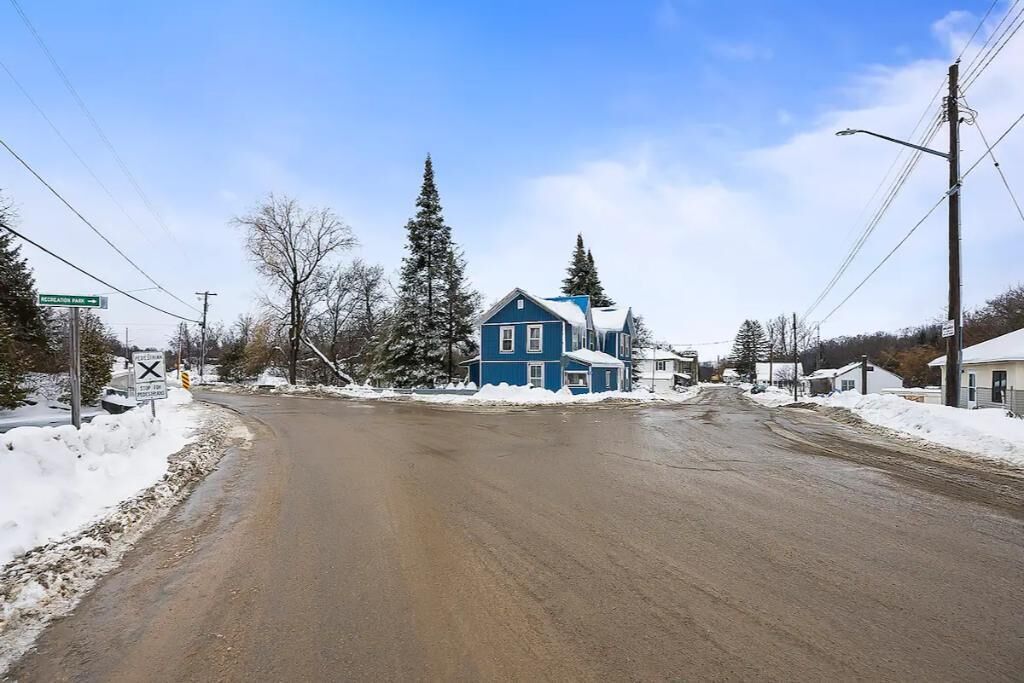 A rural road with a blue house on the left and a snow-covered landscape.