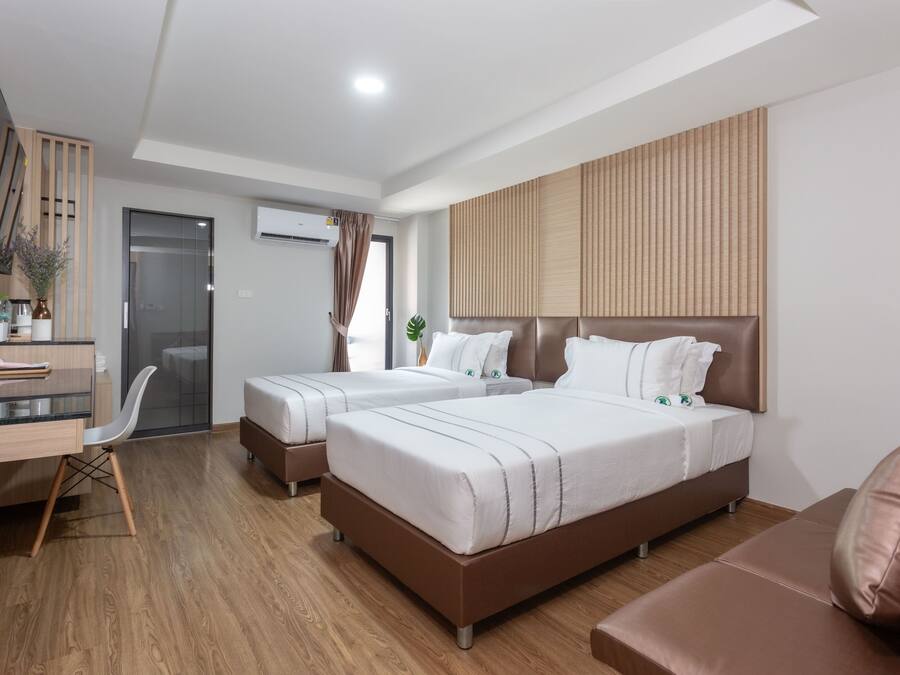 A modern hotel room with two beds, a desk, a chair, and a TV mounted on the wall.