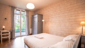 Een slaapkamer met houten vloer, een bed met witte lakens, een bureau met lamp en een kledingkast.