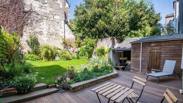 Een houten terras met buitenmeubilair, een gazon en een stenen muur.