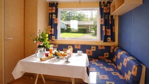 Una habitación con una mesa preparada para el desayuno, una ventana con cortinas, un banco y vistas a un jardín.