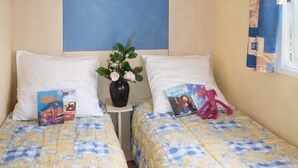 Una habitación con dos camas, un cabecero, una mesita con un florero y una ventana con cortinas.