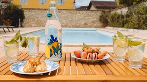 A wooden table with drinks, snacks, and a bottle by a poolside. - Lovely french house in a medieval village - private pool, ping pong & game room (Vianne)