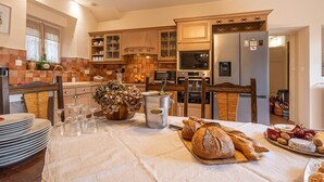 A well-lit kitchen with wooden cabinets, a dining table set with plates, glasses, and bread, and a refrigerator. - Lovely french house in a medieval village - private pool, ping pong & game room (Vianne)
