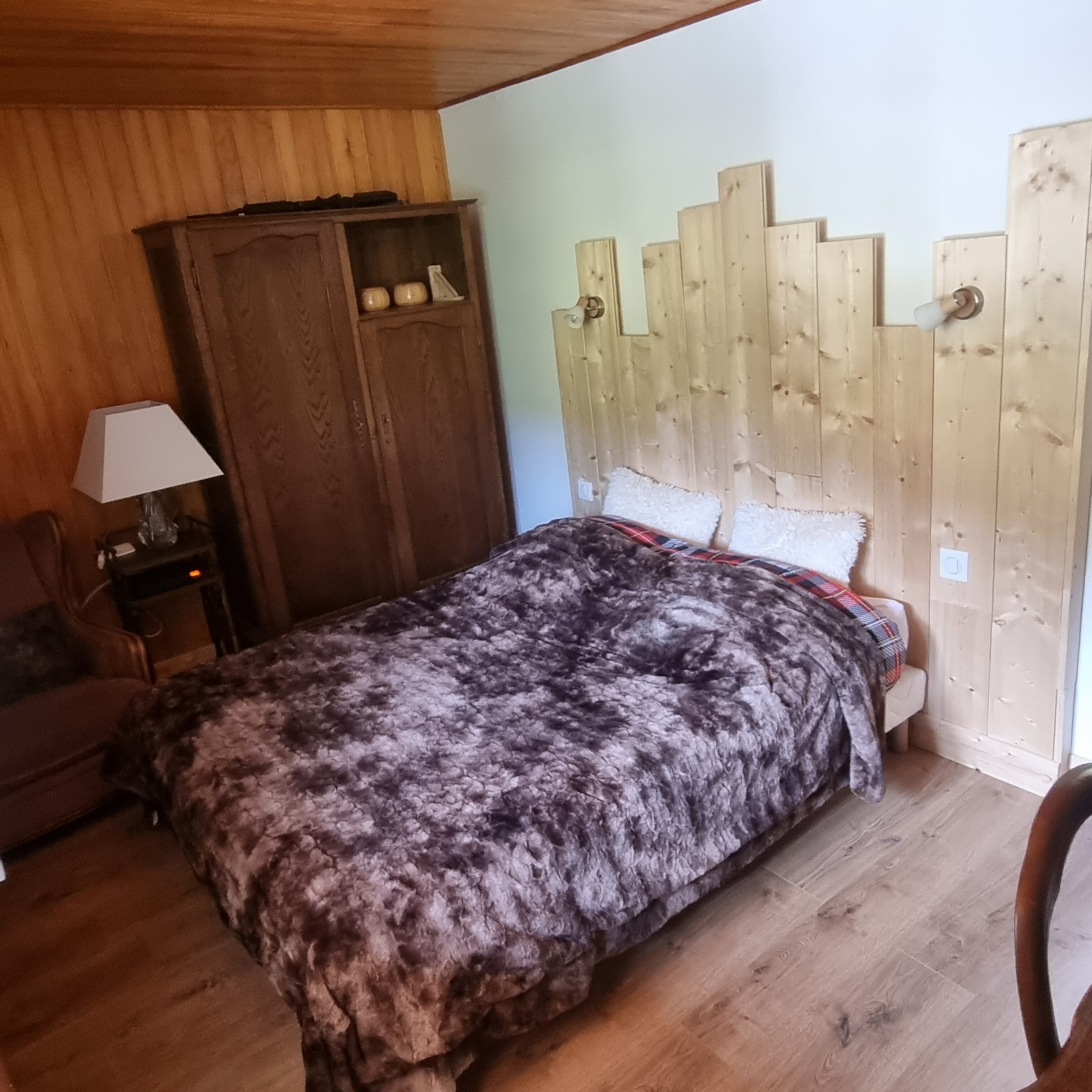 Ein Schlafzimmer mit einem Holzkopfteil, einem Bett mit gemustertem Überwurf, einem Holzschrank und einem Nachttisch mit Lampe.