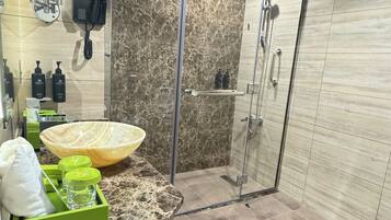 A modern bathroom with a large mirror, a glass shower enclosure, and a granite countertop with toiletries.