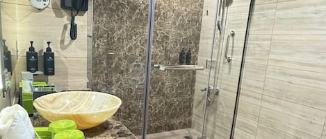 A modern bathroom with a large mirror, a glass shower enclosure, and a granite countertop with toiletries.