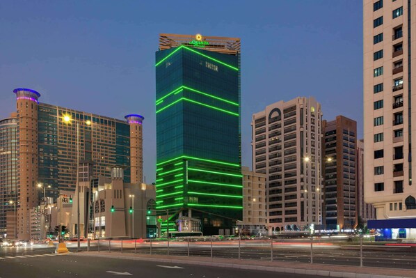 A modern high-rise building with a distinctive green-lit facade and a prominent sign at the top.