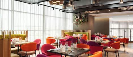 A modern restaurant with high ceilings, pendant lighting, and vibrant seating.