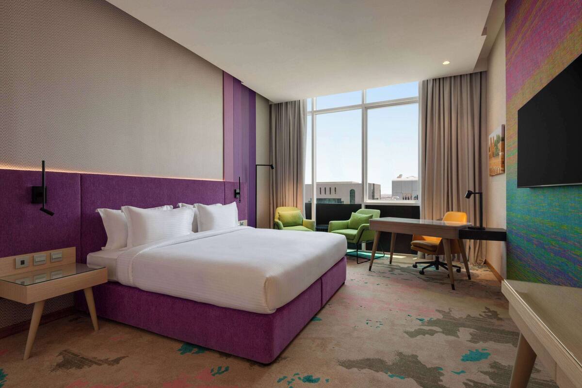 A hotel room with a large bed, a desk, a chair, and a TV.