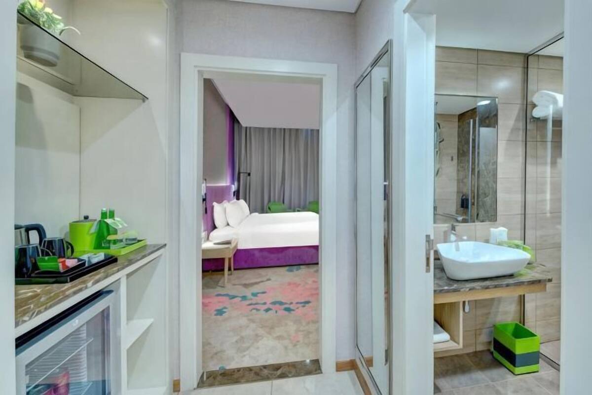A hotel room with a bed, a bathroom with a sink, and a mirror.