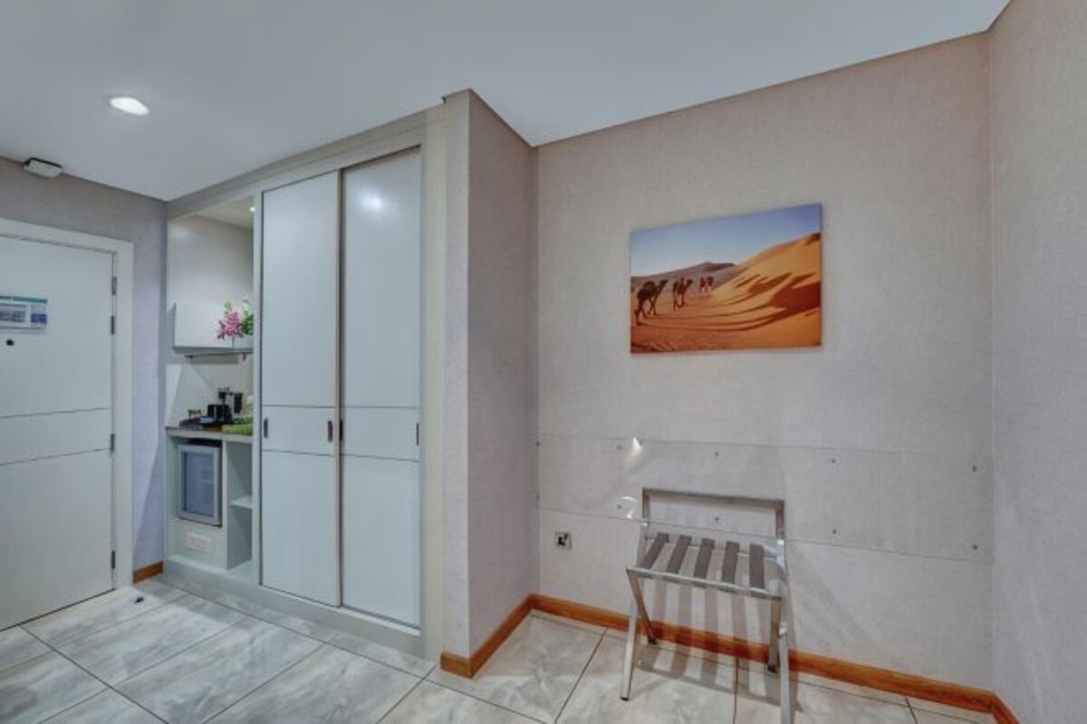 Une chambre d’hôtel avec un placard, un tableau représentant un désert et un banc.