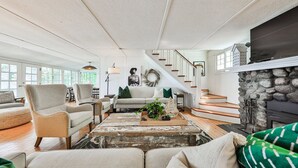 Un salon spacieux avec une cheminée, un escalier et une grande fenêtre.