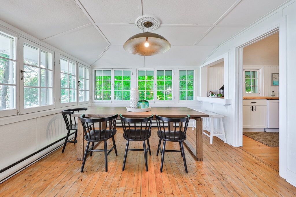 Une pièce spacieuse avec de grandes fenêtres, un plancher en bois et une table centrale entourée de chaises.