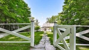 Un chemin de pierres qui mène à une maison, en passant par un portail blanc.