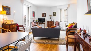A spacious living room with a dark sofa, a dining table, and a TV.