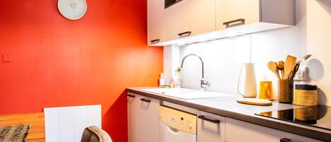 Una cocina con armarios blancos, una pared roja y un reloj.