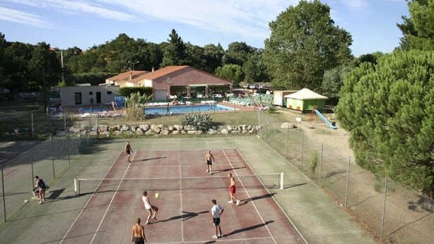 An outdoor tennis court with a pool and lounge area in the background.