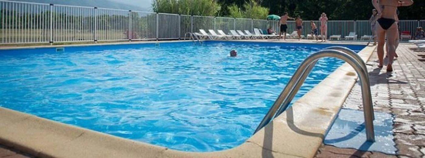 Une piscine équipée d’un escalier en métal, entourée d’une clôture et de chaises longues.