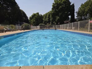 Una piscina azzurra e limpida, con bordo piastrellato, circondata da una recinzione e alberi sullo sfondo.