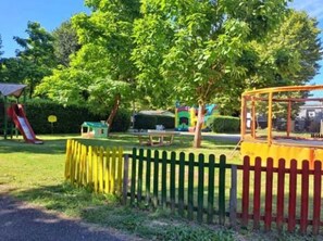 Une aire de jeux avec un toboggan, une balançoire et une zone délimitée par une clôture.