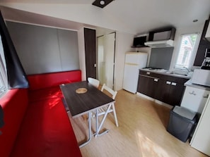 A compact kitchen with a dining area, a refrigerator, a microwave, and a trash bin. - Camping 3 étoiles - Piscine  - eeebbh (Saint-Céré)