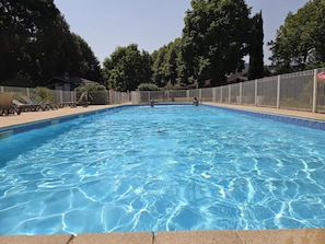 Ein klarer, blauer Pool mit einer gefliesten Kante, umgeben von einem Zaun und Bäumen im Hintergrund.