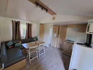 A compact living space with a sofa, dining table, chairs, a kitchenette, and a window with curtains.