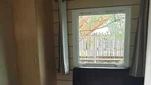 Una habitación compacta con una mesa de comedor, sillas, un sofá, un armario y una ventana que ofrece vistas a una valla y vegetación.