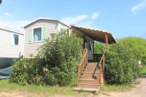 Une maison mobile de plain-pied, dotée d’une véranda et d’un escalier en bois menant à une entrée abritée.