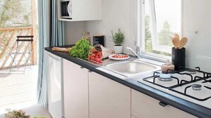A modern kitchen with a gas stove, white cabinets, and a window overlooking a balcony. - ZEcamping 3 étoiles piscine chauffée pataugeoire pet friendly locatif TV clim (Roquebrune-sur-Argens)