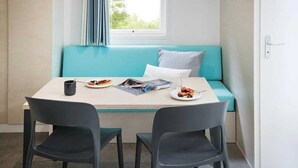 A small dining area with a table, two chairs, a blue sofa, and a window with curtains. - ZEcamping 3 étoiles piscine chauffée pataugeoire pet friendly locatif TV clim (Roquebrune-sur-Argens)
