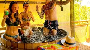 A wooden hot tub with people enjoying the water, a colorful tablecloth, and a straw hat on the table. - ZEcamping 3 étoiles piscine chauffée pataugeoire pet friendly locatif TV clim (Roquebrune-sur-Argens)