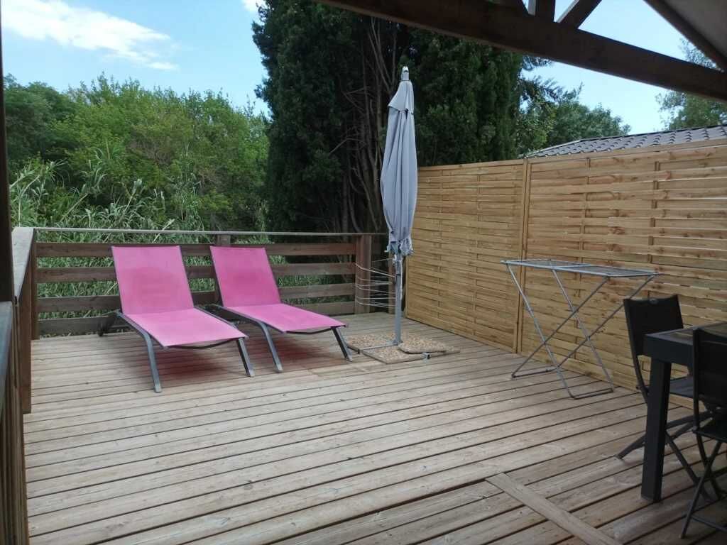 Eine Terrasse im Freien mit zwei rosa Liegestühlen, einem Tisch und einem Klappstuhl.