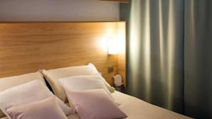 Una camera d'albergo con un letto, un comodino, una lampada e una finestra con tende.
