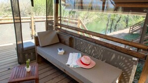 Una terraza de madera con zona de estar acolchada, una mesita con una planta y vistas al bosque circundante.