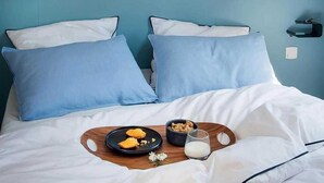 Une chambre avec deux lits, une tête de lit en bois, une étagère avec des objets décoratifs et une table de chevet avec une lampe.