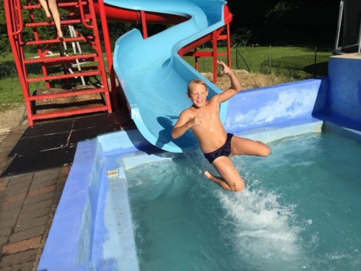Eine Person im Swimmingpool bei einer blauen Rutschenanlage.
