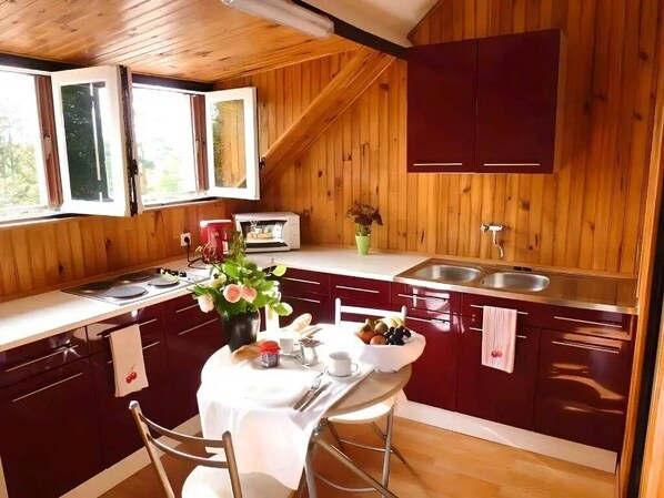 Une cuisine compacte aux murs en bois, dotée d’un plan de travail blanc et d’un coin repas avec une table dressée pour deux personnes.