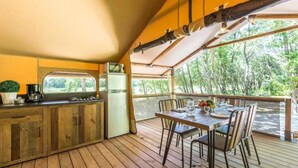 A wooden deck with a table and chairs, a small kitchen area with a refrigerator and coffee maker, and a view of trees through the open sides. - ZEcamping 3 étoiles piscine chauffée pataugeoire locatif TV clim 34m2 (Roquebrune-sur-Argens)